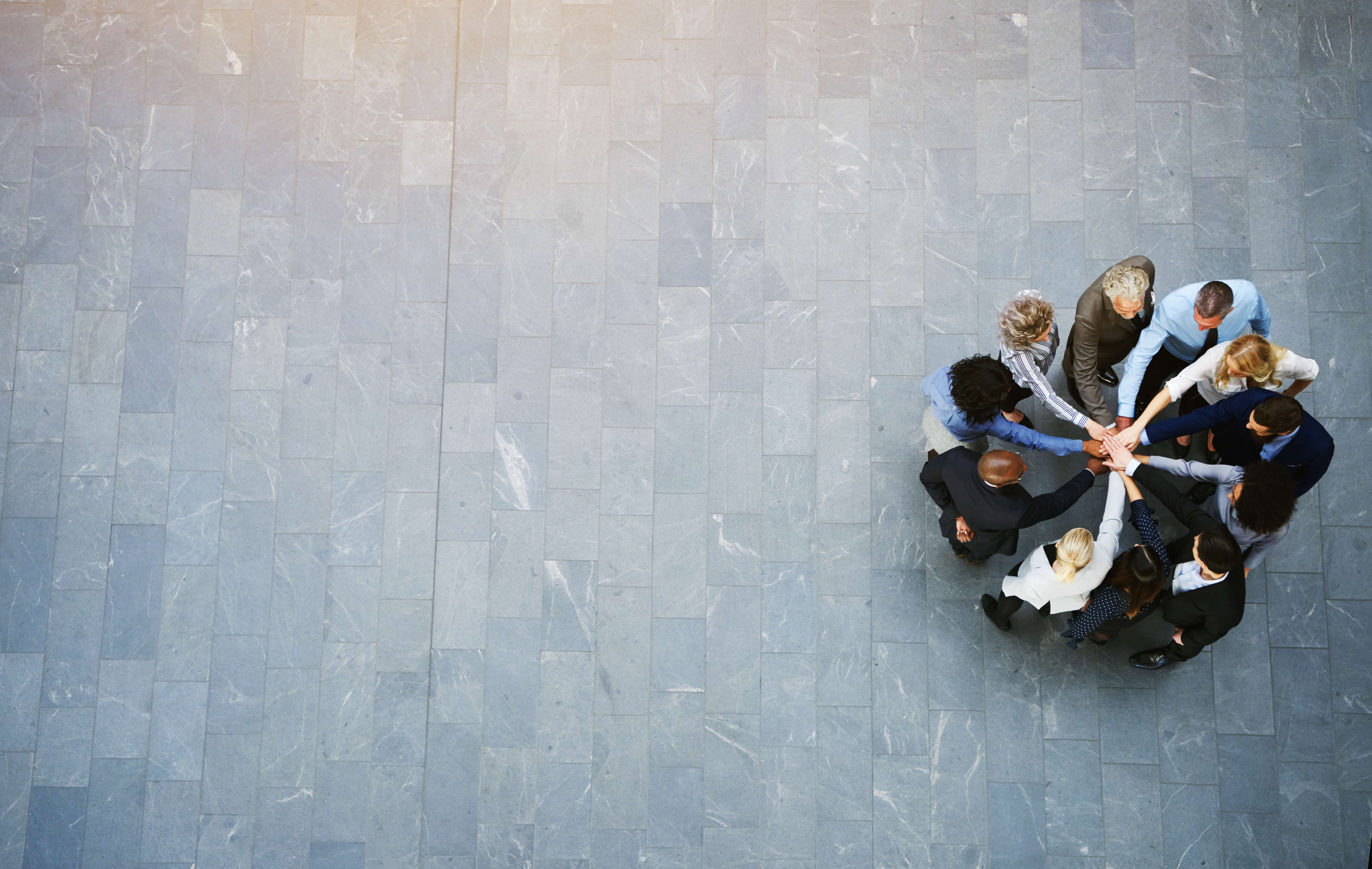 Overhead image of a group of people standing in a circle with their hands in the middle of the circle.